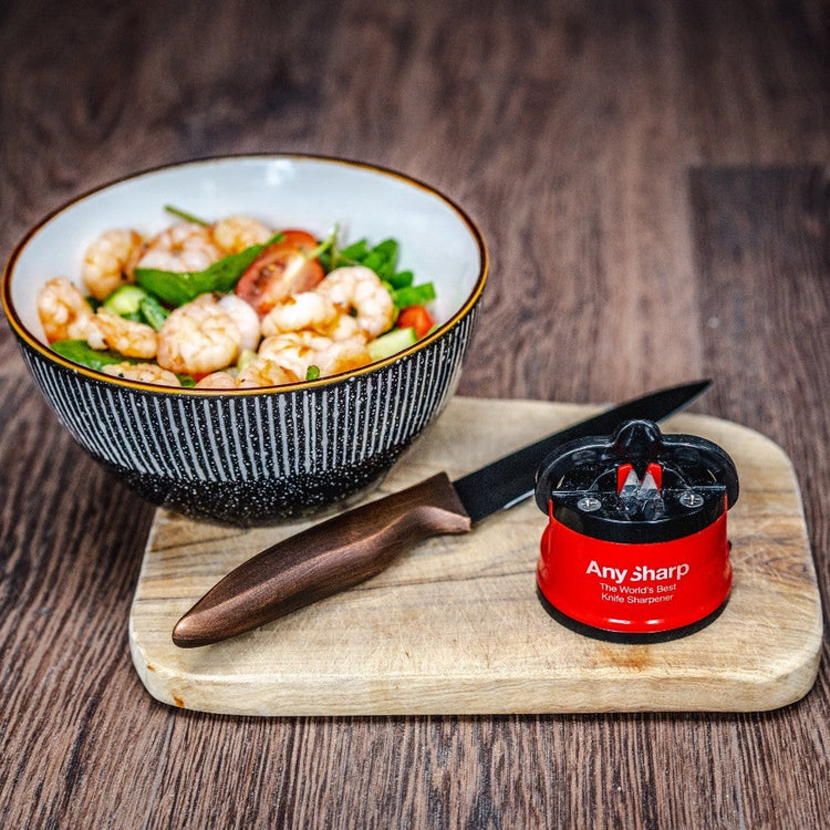 Bowl of salad with a knife and sharpener on a wooden surface