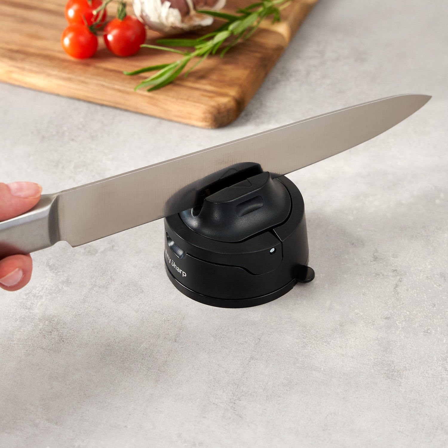 Knife being sharpened on a black sharpener with a cutting board and vegetables in the background.