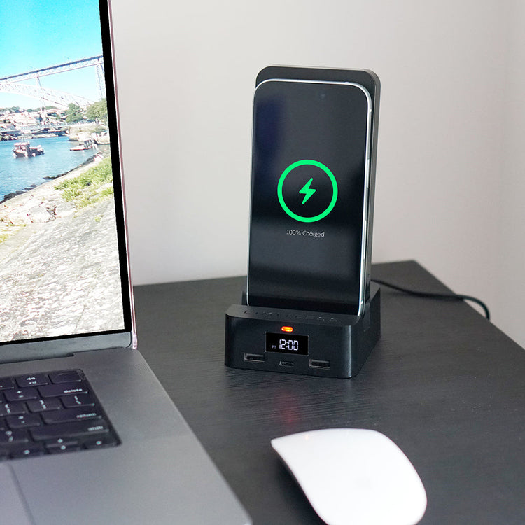 Phone charging dock with digital clock on a desk next to a laptop