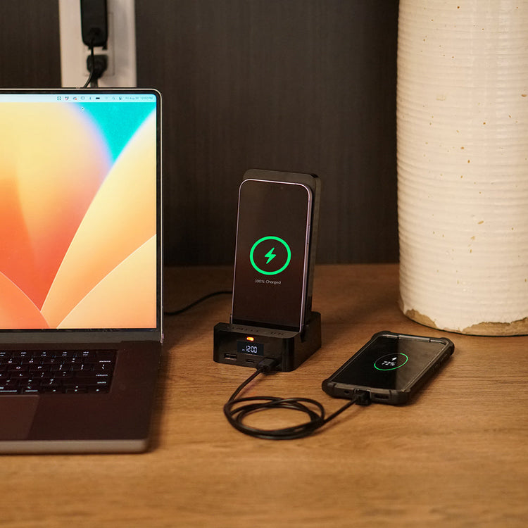 Laptop and smartphone on a wooden surface with wireless charging pad and phone.