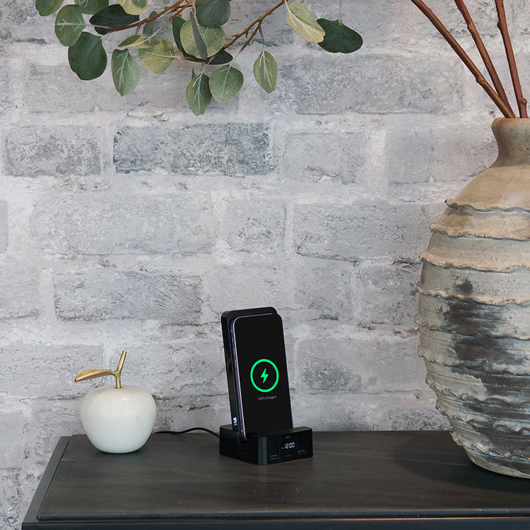 Wireless charger on a table with decorative items against a stone wall.