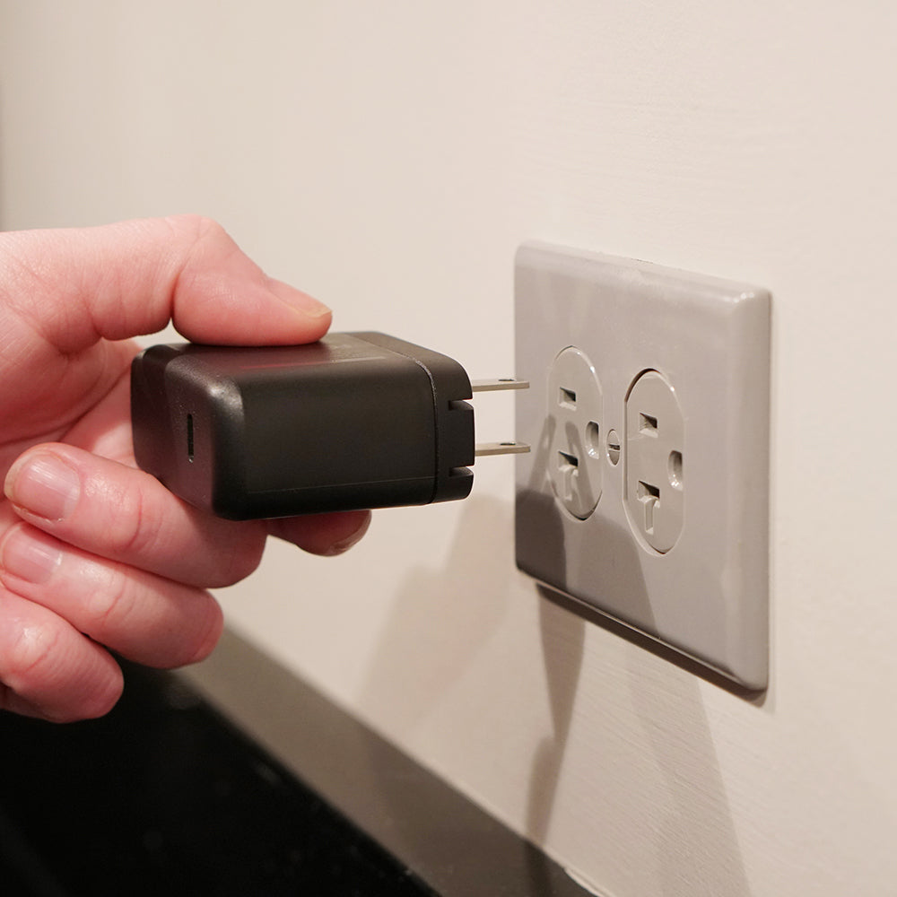 Hand plugging a black adapter into a wall socket.