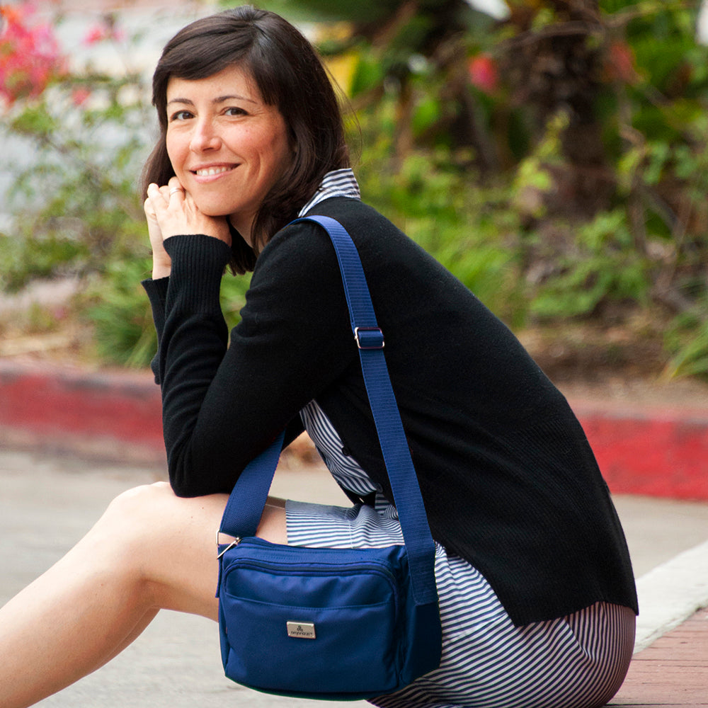 A person seated on a bench with a striped skirt and a black top, wearing a blue crossbody bag with multiple compartments.