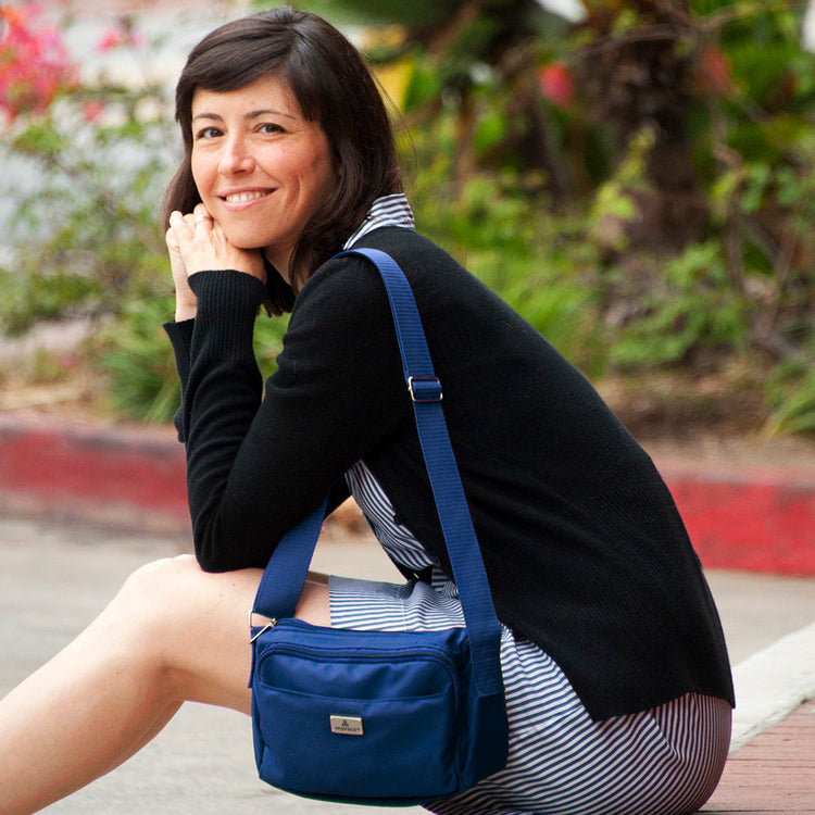 A person seated on a bench with a striped skirt and a black top, wearing a blue crossbody bag with multiple compartments.