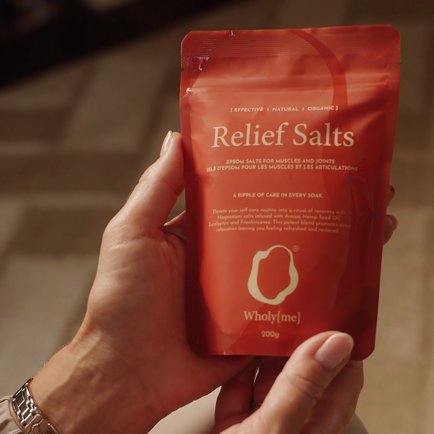 Hand holding a red package of 'Relief Salts' by Wholy Me against a blurred background