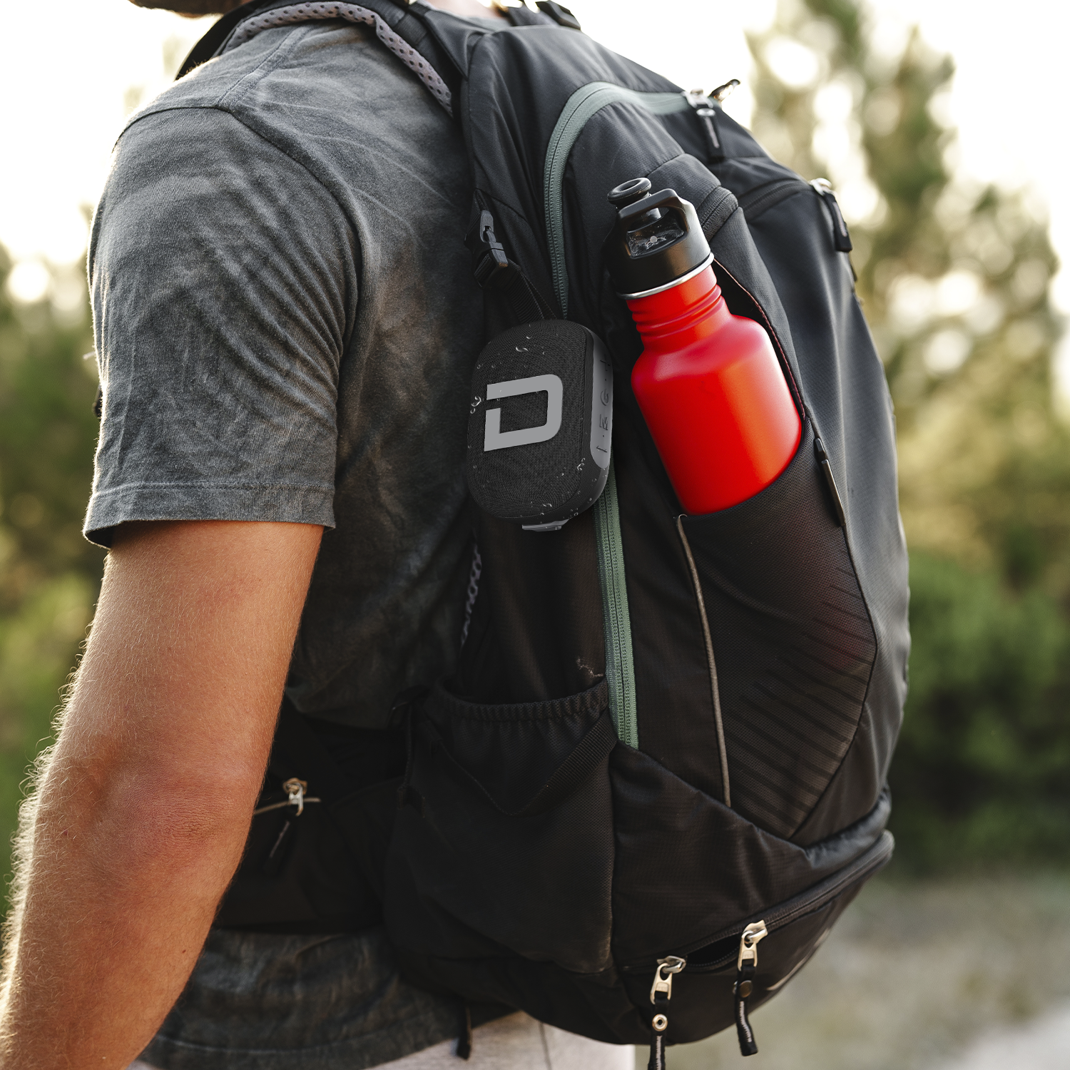 Person wearing a black backpack with a red water bottle, outdoors.