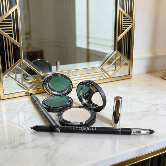 Makeup products including compacts and a pencil on a marble surface with a decorative mirror in the background.