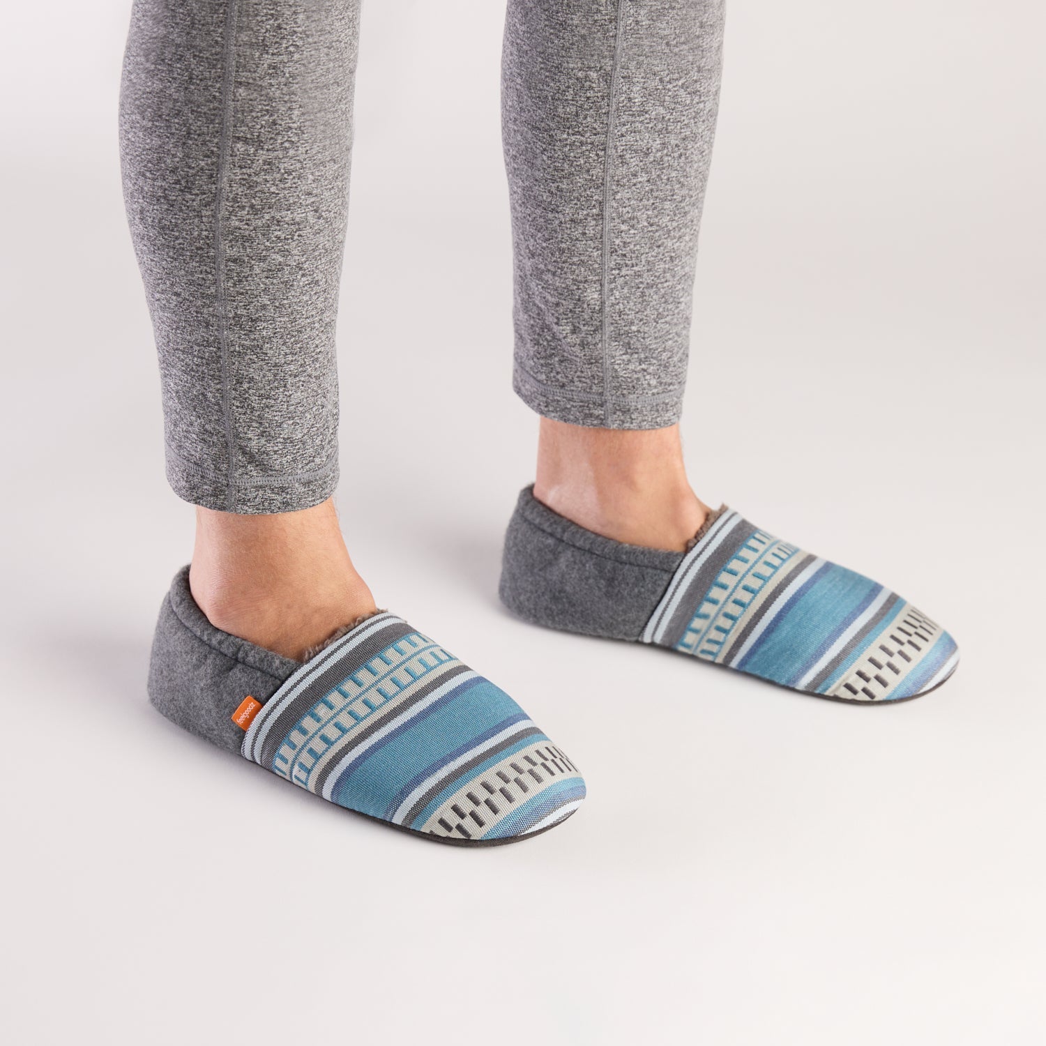 Gray slippers with blue pattern worn by a person on a white background