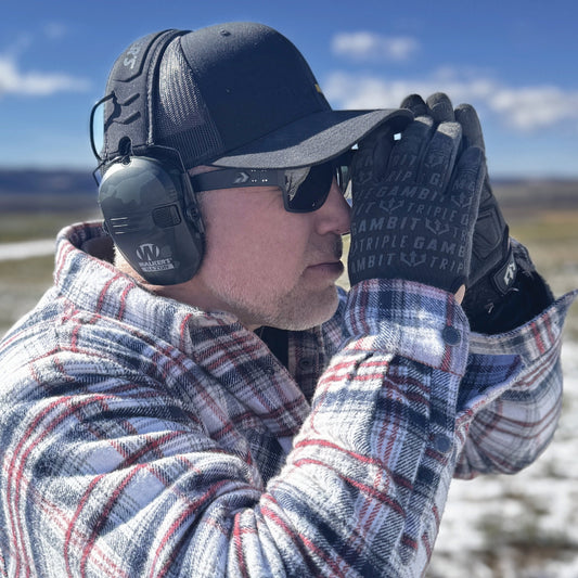 Man wearing ear protection, sunglasses, and gloves outdoors with a clear sky.