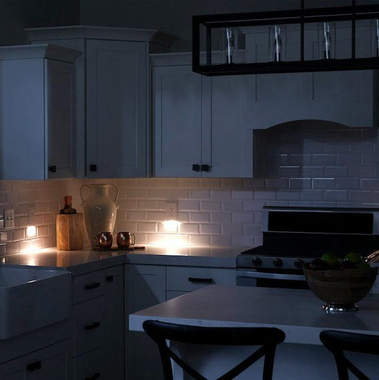 A white 2-pack of GuideLight outlet cover plates with built-in LED lights, mounted on a blue wall with the outlets visible at the bottom.