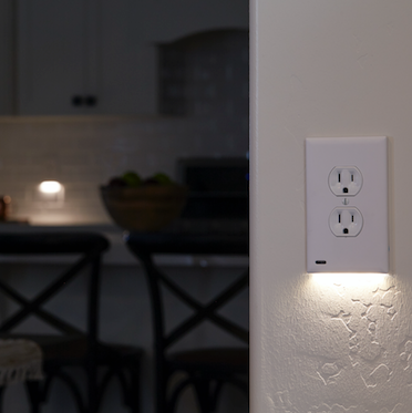 A white 2-pack of GuideLight outlet cover plates with built-in LED lights, mounted on a blue wall with the outlets visible at the bottom.