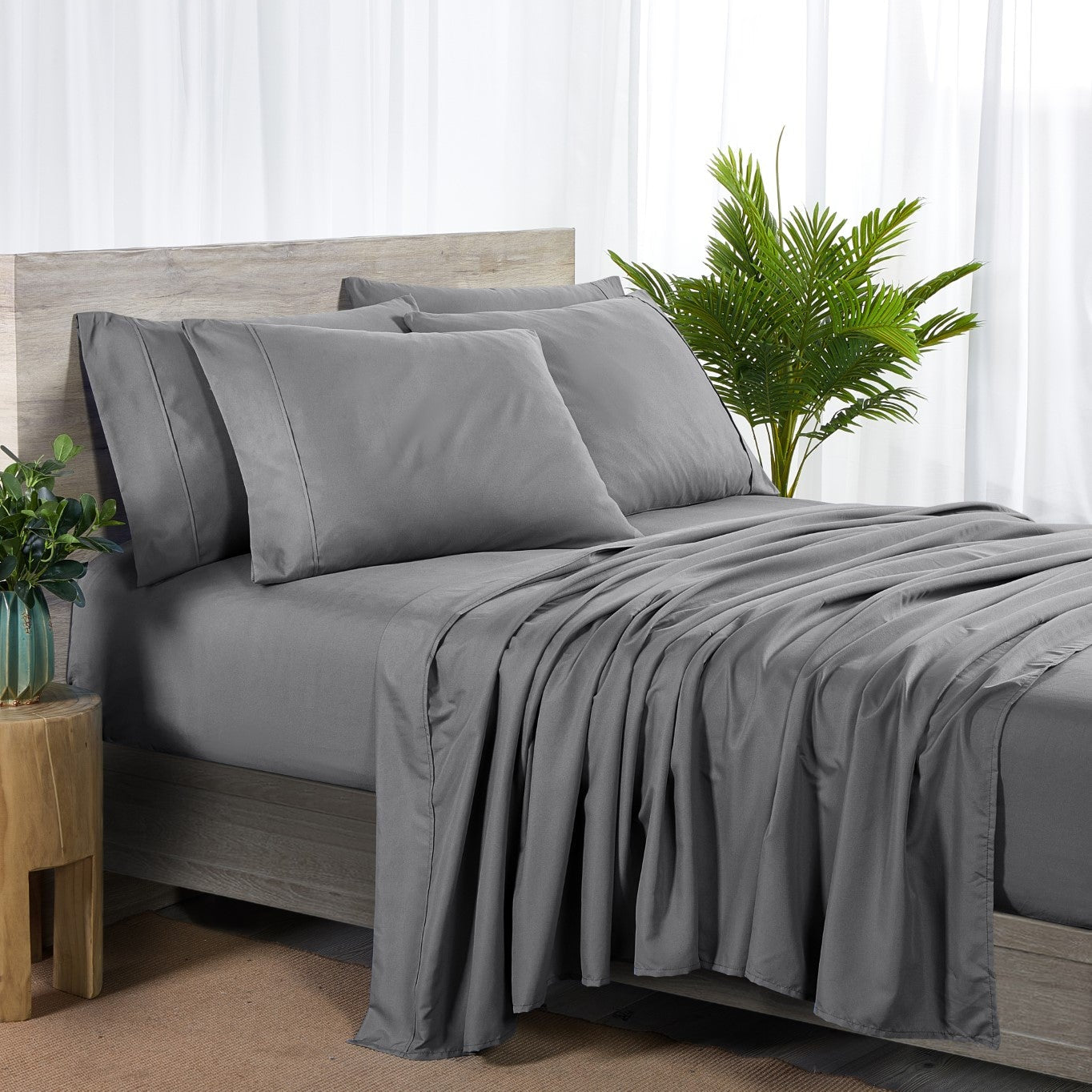 Gray bedding set on a bed with a wooden headboard and plants in the room.