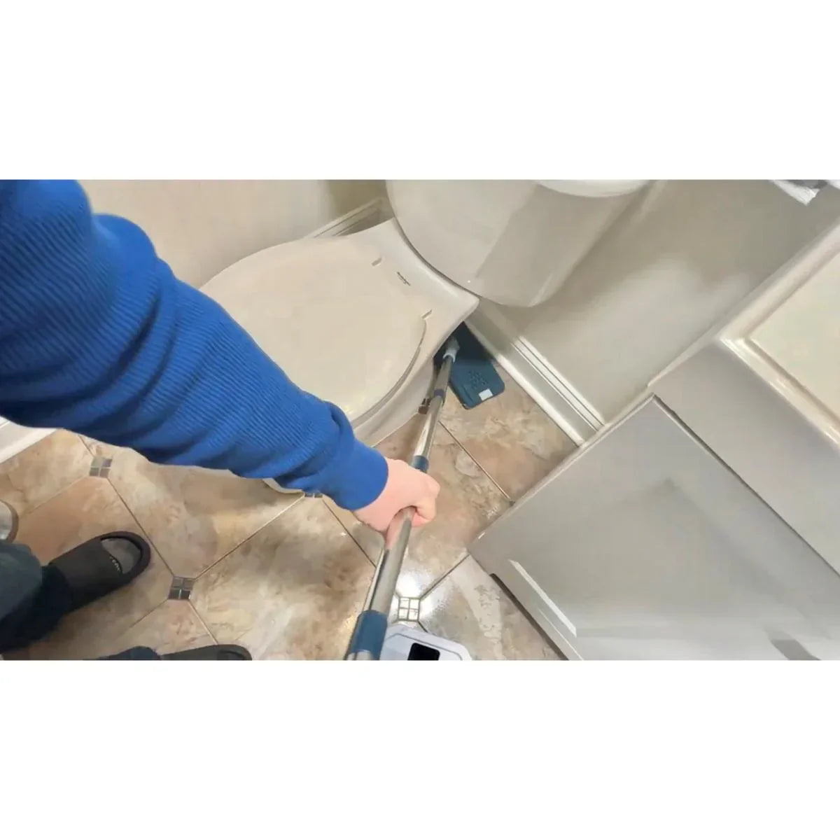 Person cleaning a bathroom floor with a mop, wearing a blue sweater.