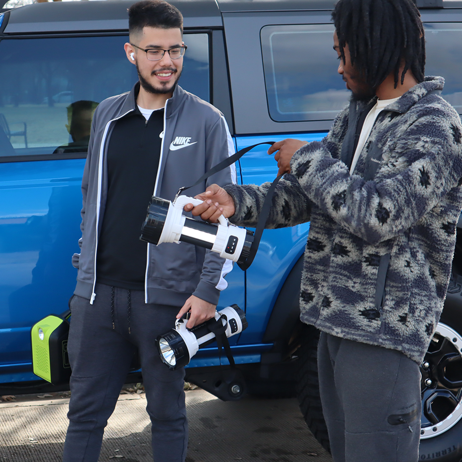 Two men exchanging a device in front of a blue vehicle