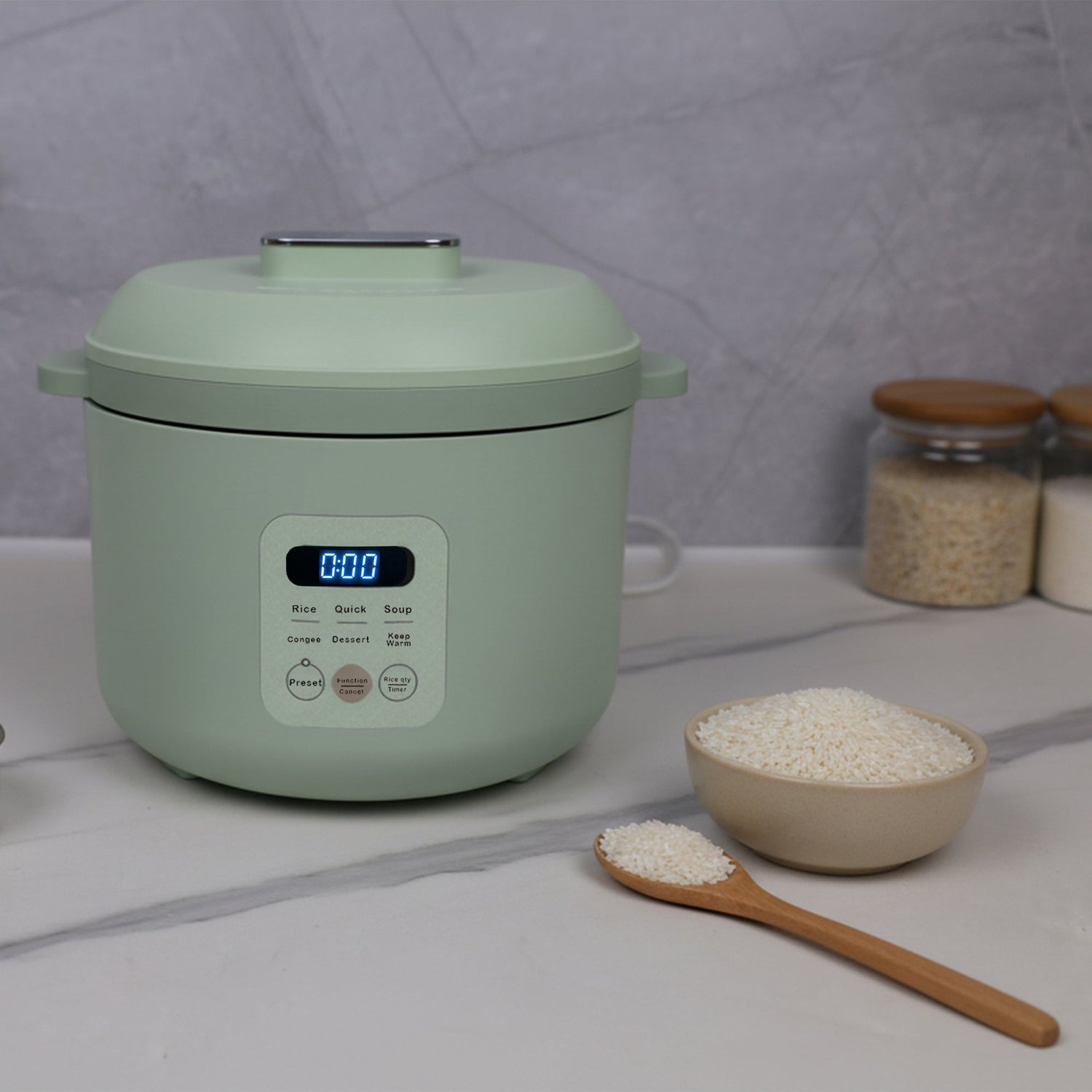 Green rice cooker with a bowl of rice and wooden spoon on a light gray surface.