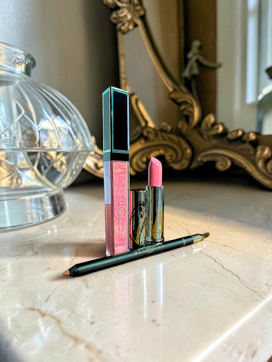 Lipstick, lip gloss, and lip liner on a marble surface with a decorative mirror in the background.
