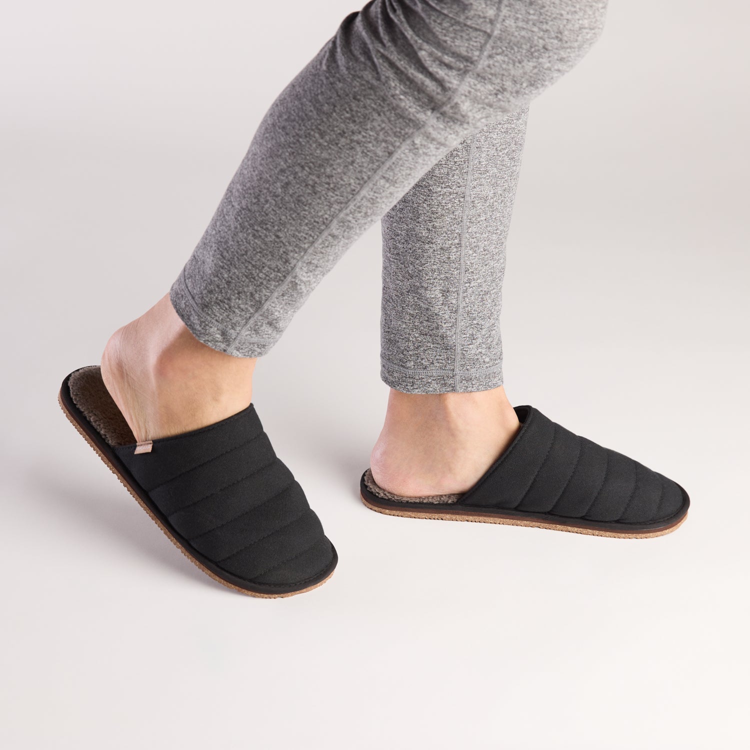 Person wearing black slippers on a light gray background