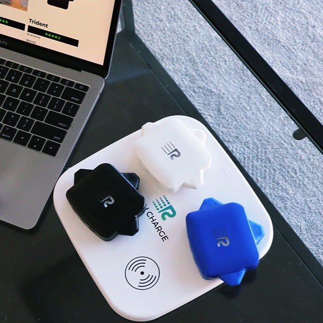 Wireless charging pad with electronic devices on a desk next to a laptop.