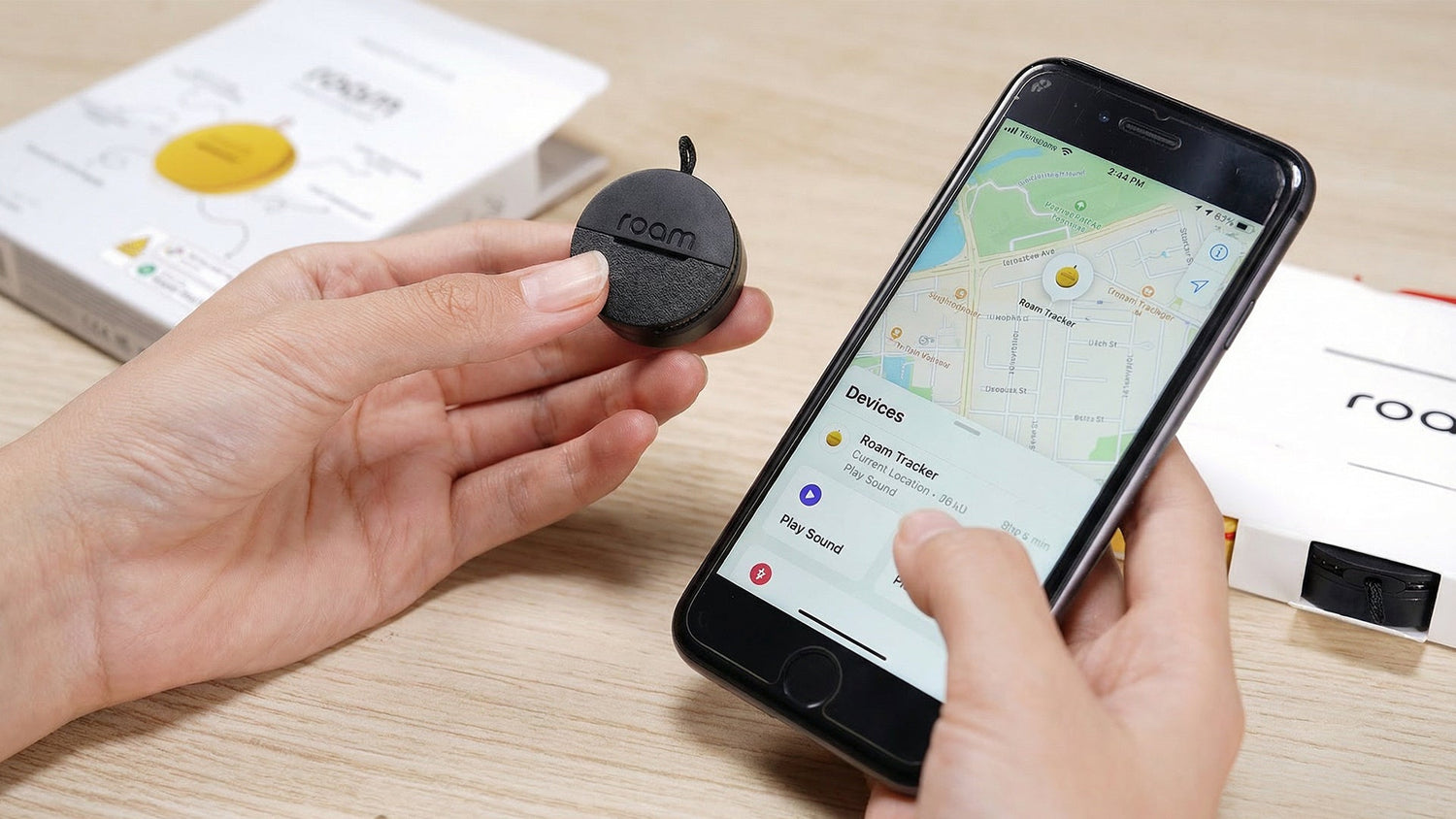 Person holding a small device next to a smartphone displaying a map app on a wooden surface.