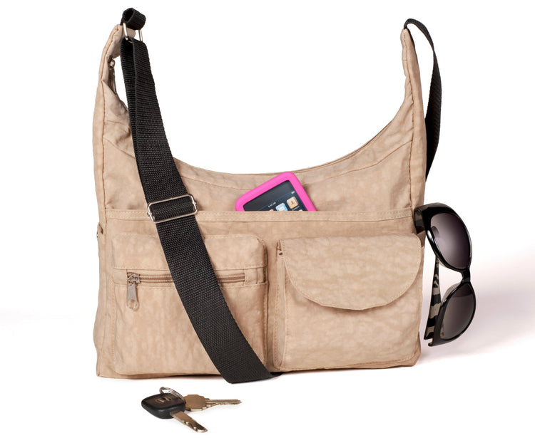 Beige shoulder bag with black strap, sunglasses, keys, and a pink item on a white background