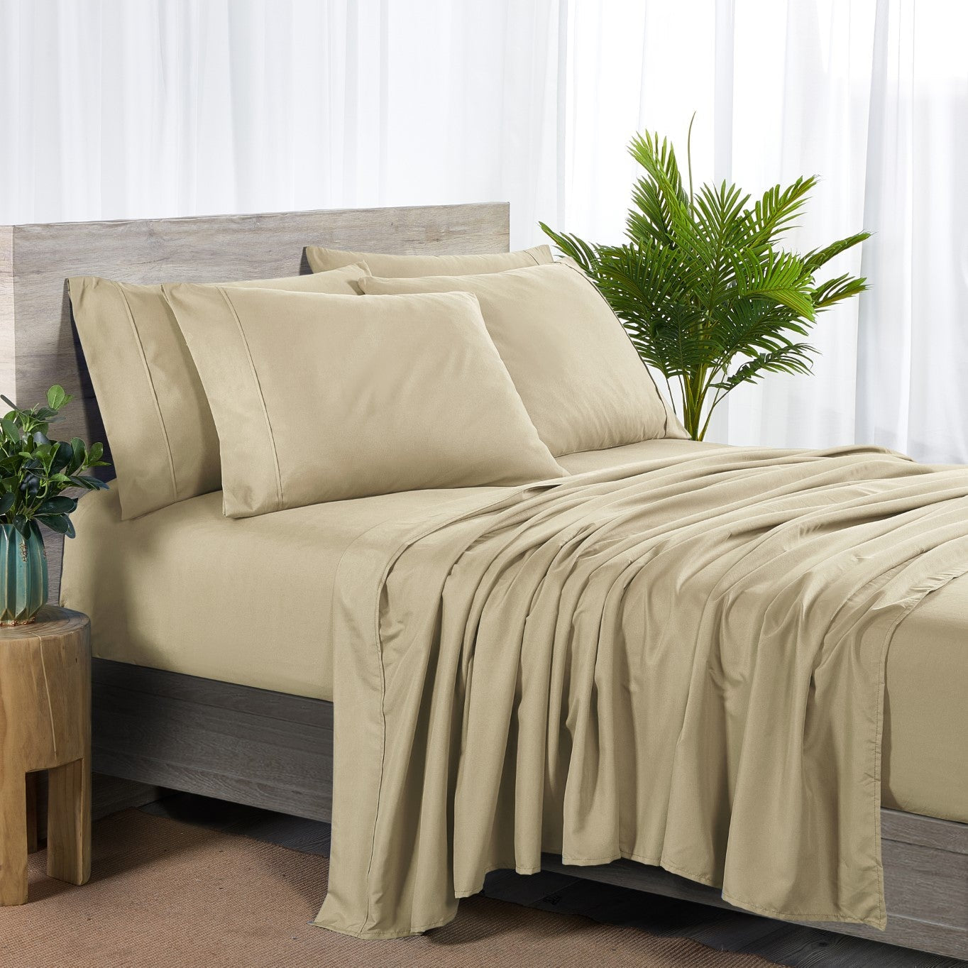 Beige bed sheets and pillows on a bed with a plant and side table in the background.