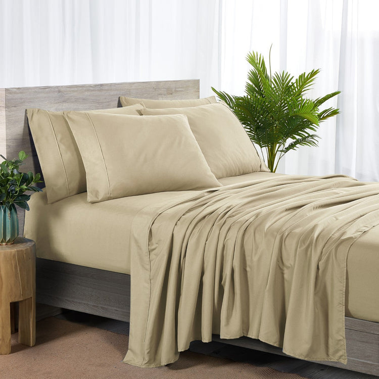 Beige bed sheets and pillows on a bed with a plant and side table in the background.