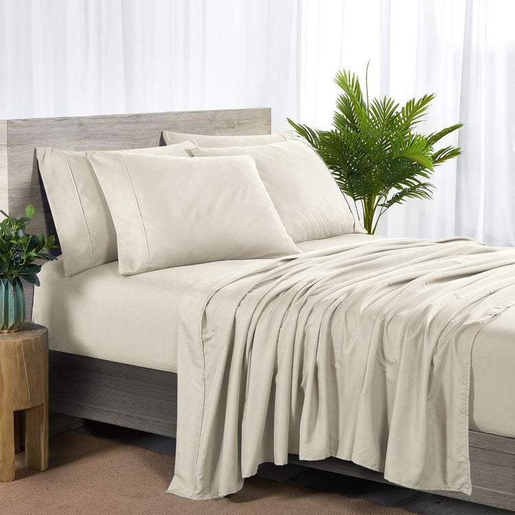 Beige bedding set on a bed with a wooden headboard and plant decor.