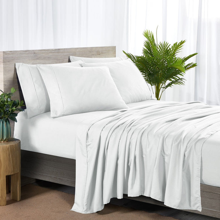 White bedding set on a bed with a wooden headboard and plants in the background.