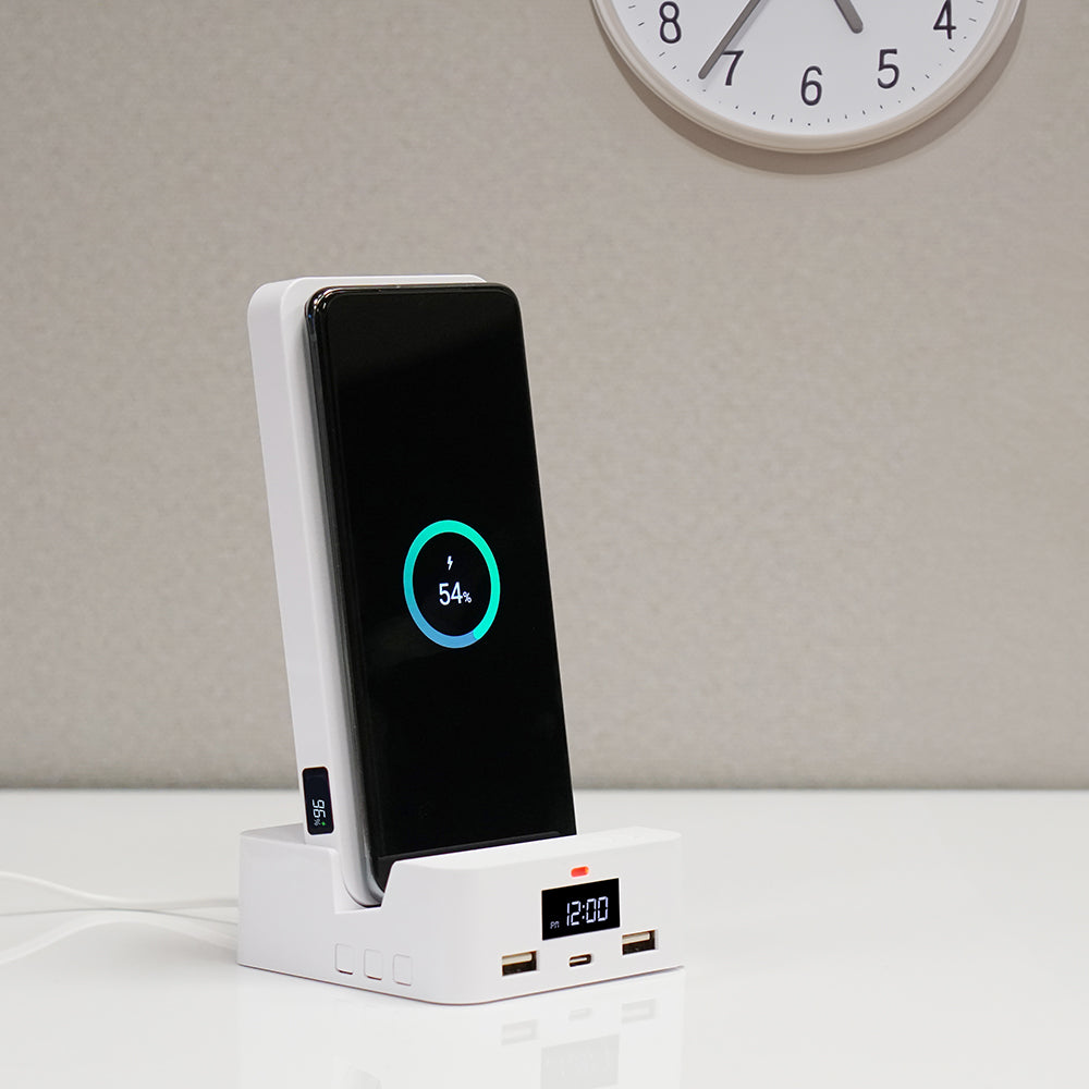 White charging station with smartphone on a light gray surface, clock in the background