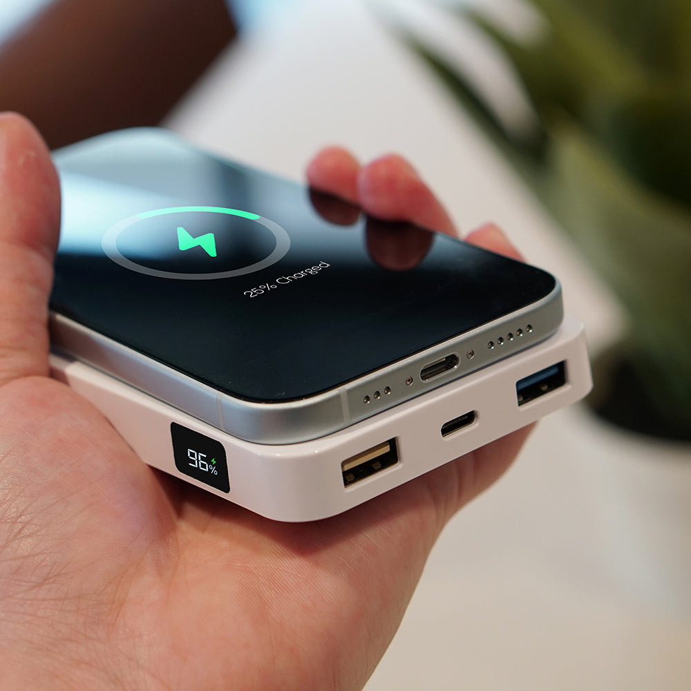 Hand holding a power bank with smartphone on top, displaying charging status.