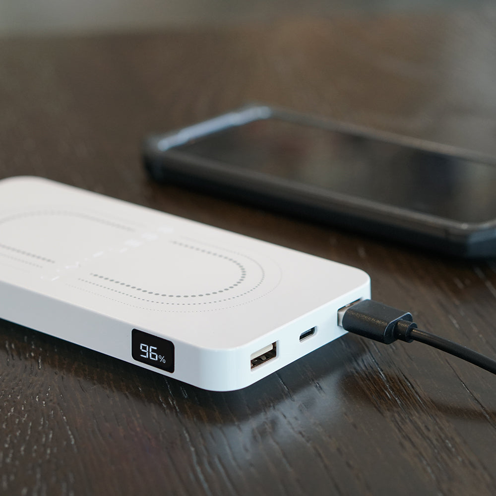 White power bank with digital display on a wooden surface, connected to a smartphone.