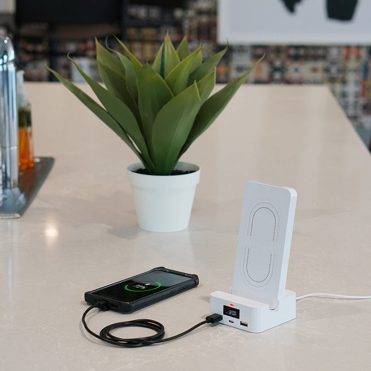 Wireless charging station with smartphone on a table next to a potted plant