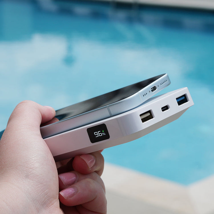 Hand holding a power bank with a pool in the background