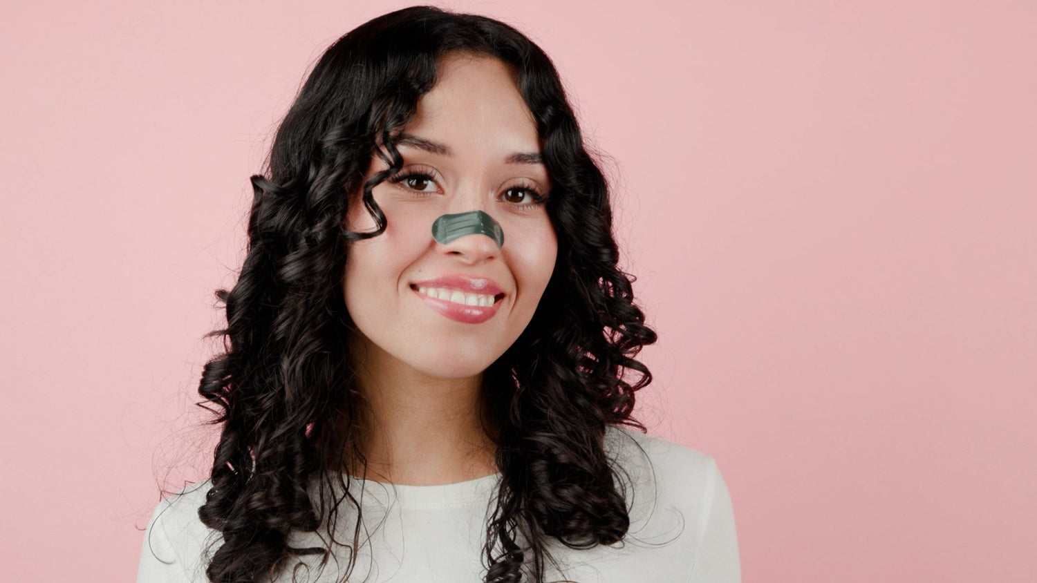 Woman with a green leaf on her nose against a pink background