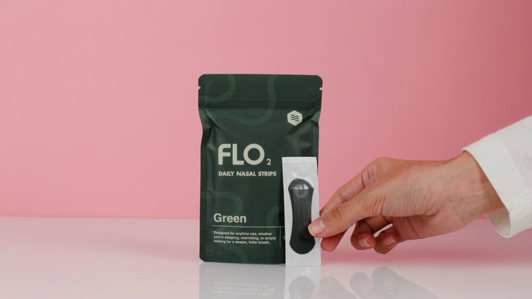 Hand holding a green package of FLO2 baby nasal strips against a pink background