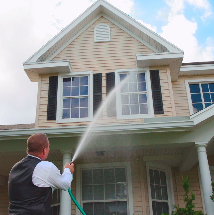 Person washing a house with a hose on a clear day
