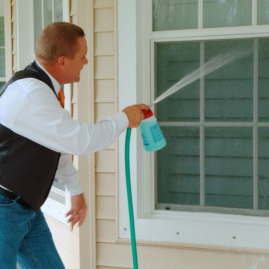 Person washing a house with a hose on a clear day