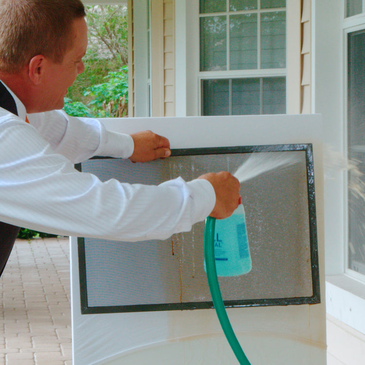 Person cleaning a window screen with a spray bottle outdoors.