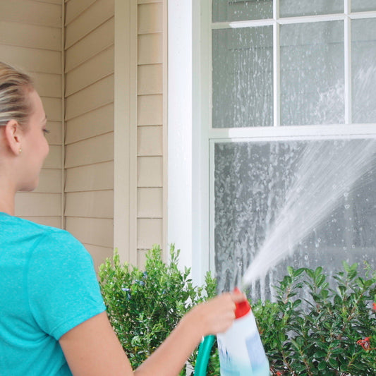 Person washing a house with a hose on a clear day