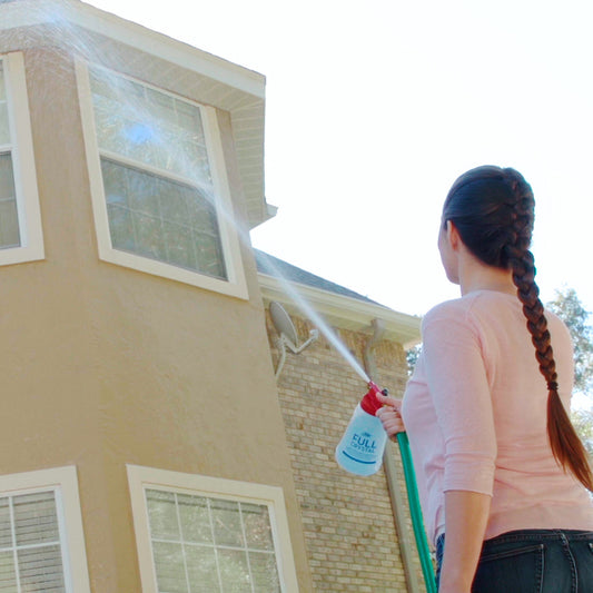 Person washing a house with a hose on a clear day