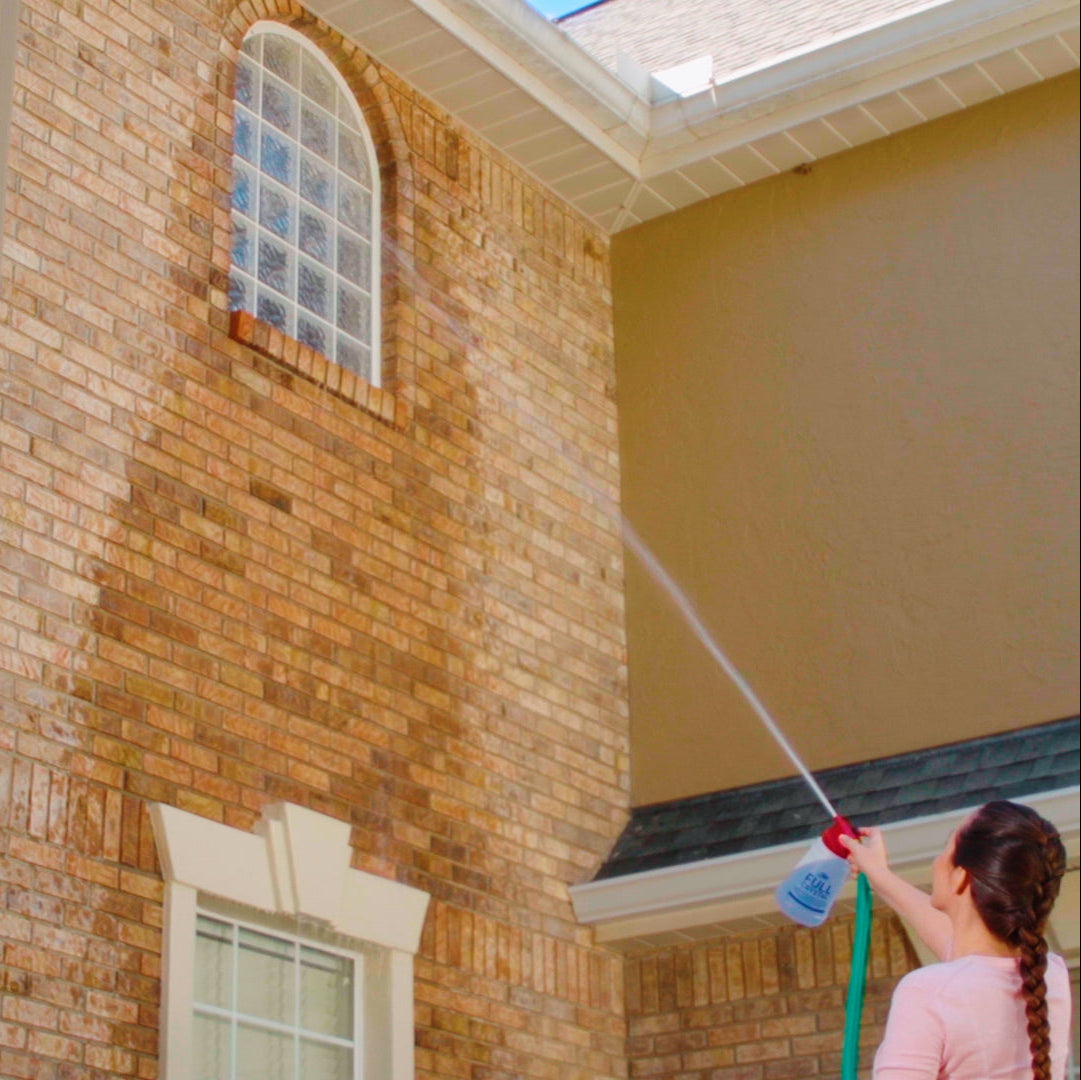 Person cleaning a brick building with a pressure washer.