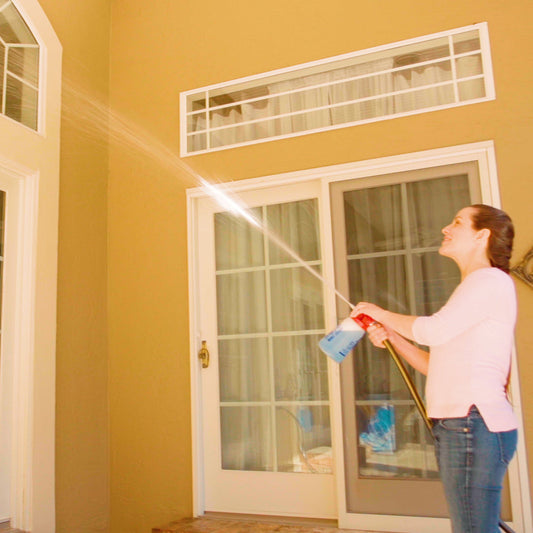 Person washing a house with a hose on a clear day