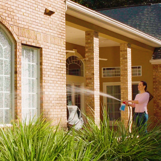 Person washing a house with a hose on a clear day
