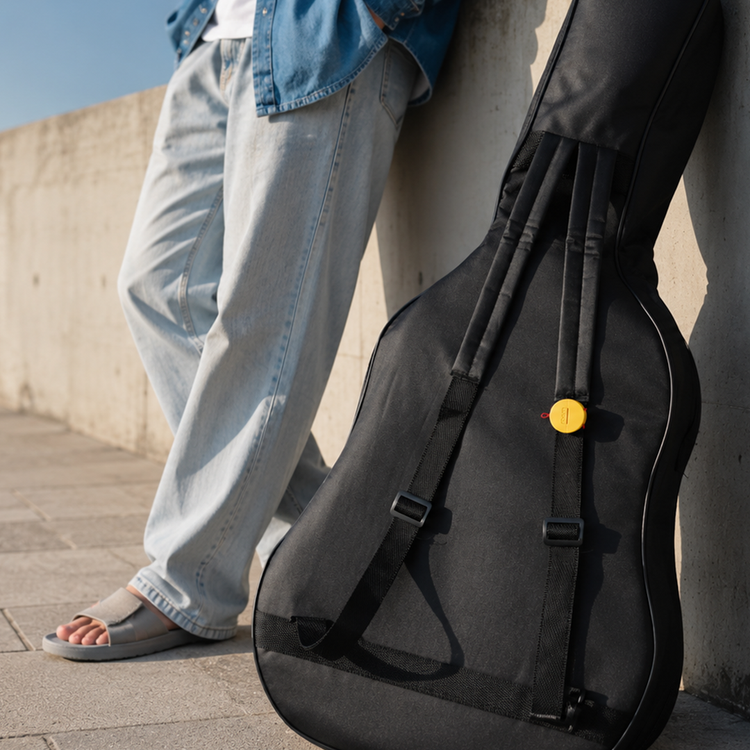 Person holding a black guitar case with a yellow button on a concrete surface.