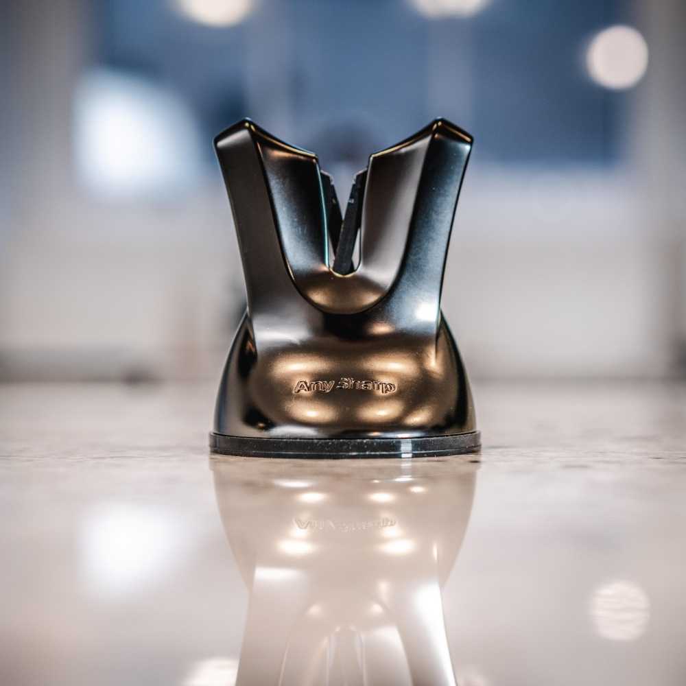Metallic kitchen knife sharpener on a reflective surface with a blurred background