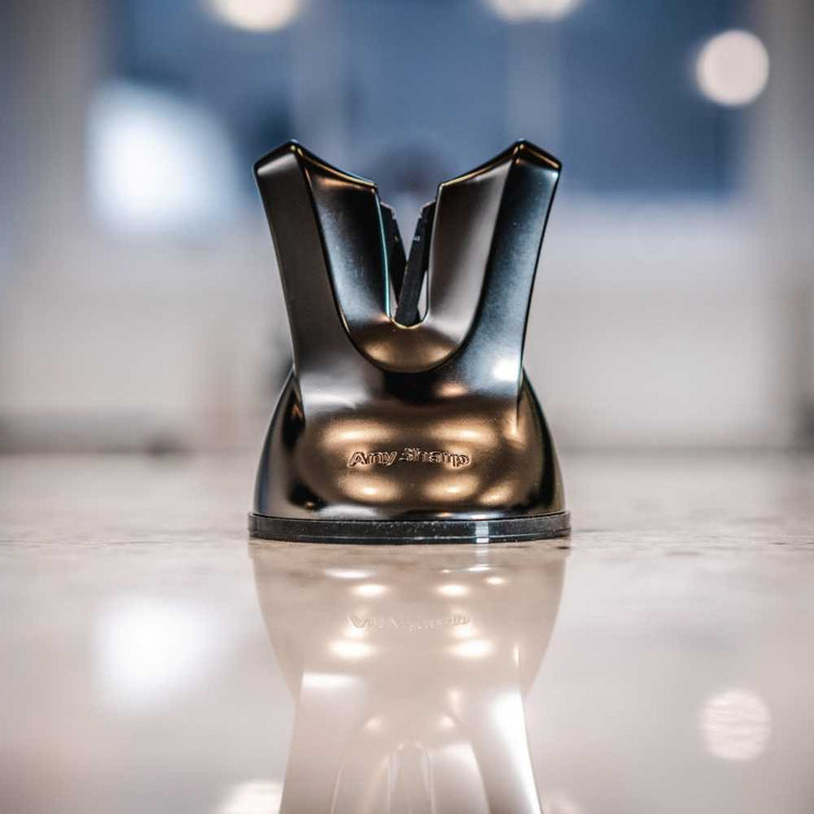 Metallic kitchen knife sharpener on a reflective surface with a blurred background